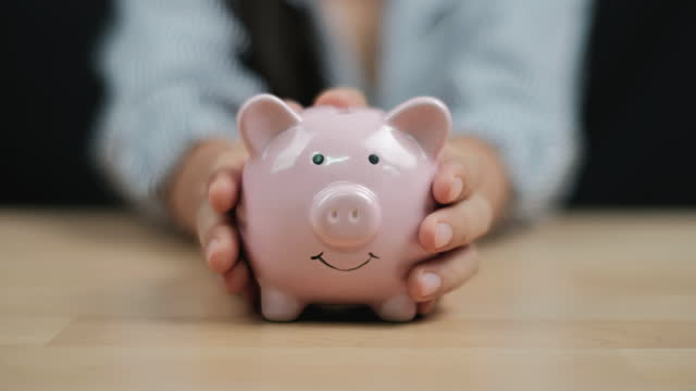 Saving money concept, Women hand hold a piggy bank on wooden table. Close up.