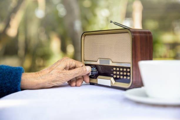 main aînée de femme tournant le bouton sur la radio de cru dans l’arrière-cour. - woman taking radio vintage photos et images de collection
