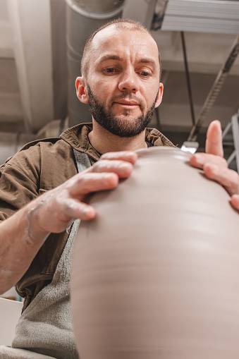 Potter making a huge jug of white clay on the potter's wheel circle in studio, concept of creativity and art, vertical photo