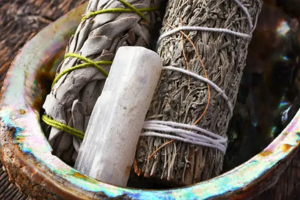 A close up image of two white sage smudge sticks with selenite crystal in an abalone shell.