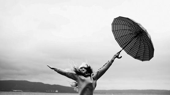 Young adult woman bouncing with umbrella in rainy weather, black and white photo