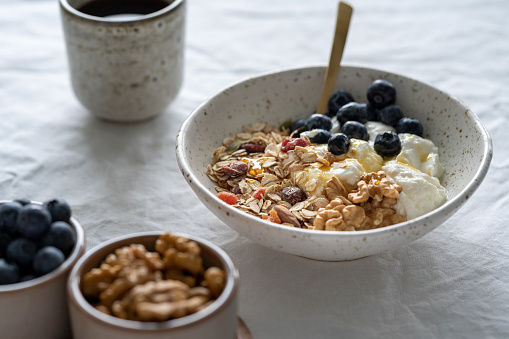 Healthy lifestyle breakfast with granola muesli and yogurt in bowl on white table background, cereal grain food with nuts seed. Organic morning diet meal with oat for health care. Against window