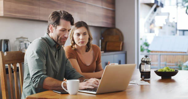 And so the tax season begins Shot of a young couple using a laptop while going over their finances together at home tax season photos stock pictures, royalty-free photos & images