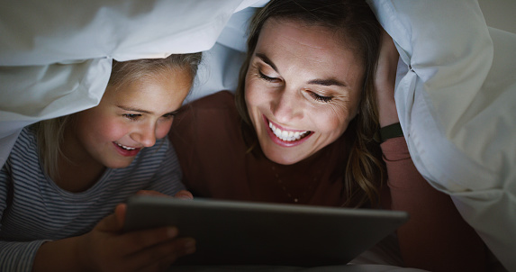 Shot of an adorable little girl using a digital tablet with her mother at bedtime