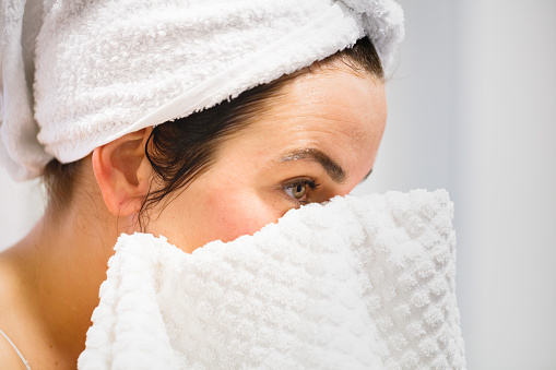 Close side view of woman wearing a towel on head after shower, drying her face with white towel