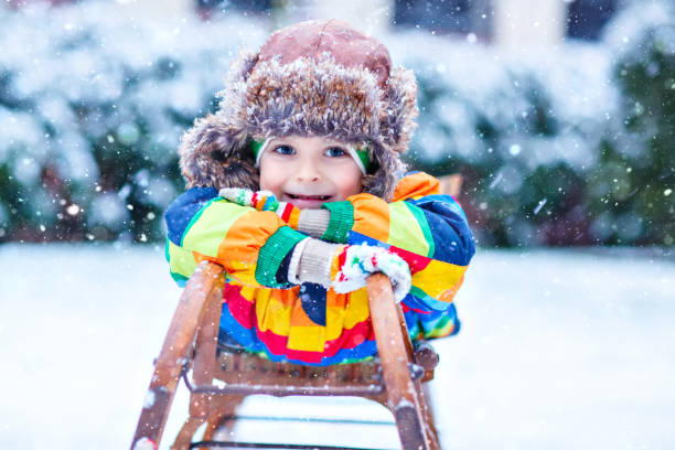 �маленький мальчик, наслаждаясь ездой на санях во время снегопада. счастливый ребенок дошкольного верхом на старинных санях. - little boys sled clothing slide стоковые фото и изображения