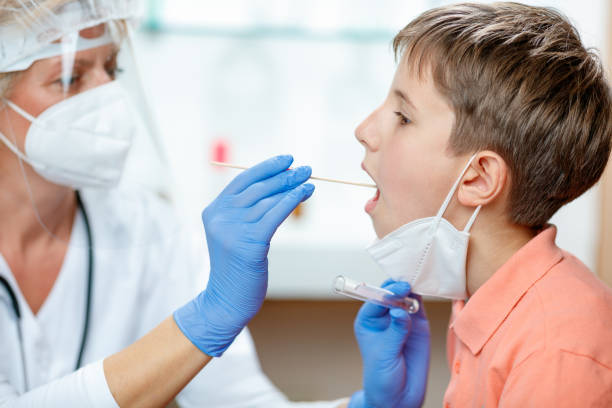 istock Female doctor in protective workwear taking swab sample from boy's mouth 1289841320