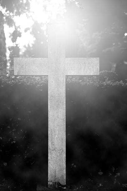 istock Old stone cross tombstone in a graveyard with bright backlight and fog. 1289845144