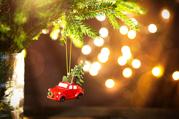 Christmas decor - red retro car carries Christmas tree with gift boxes on roof. space for text. New Year. Toy on branch of fir tree with Golden lights of garlands in defocus, bokeh, holiday background