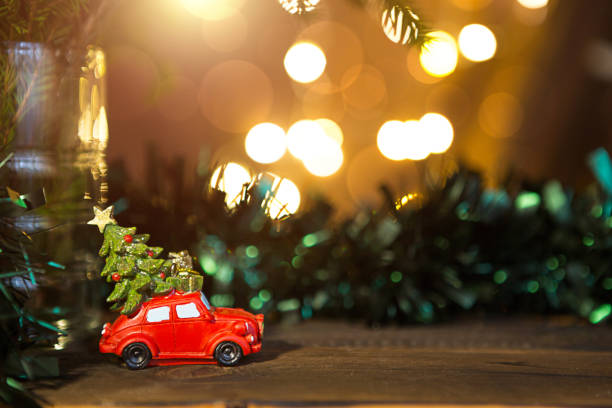 istock Christmas decor - red retro car carries Christmas tree with gift boxes on roof. space for text. New Year. Toy on branch of fir tree with Golden lights of garlands in defocus, bokeh, holiday background 1289845909