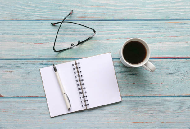 istock Open notepad with pen, spectacles and coffee on blue wood table. Top view. 1289849744