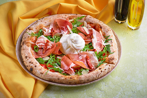 Food concept. Fresh original Italian Pizza with burrata, prosciutto and arugula on light table. Concept of healthy eating for menu.