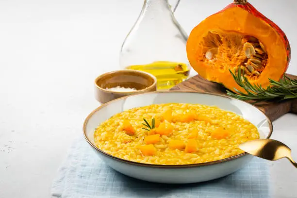 Pumpkin risotto on white table. Close-up. Raw pumpkin on background. Copy space.