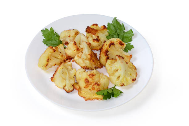 Pieces of a blanched cauliflower fried in batter and decorated with parsley leaves on dish on a white background