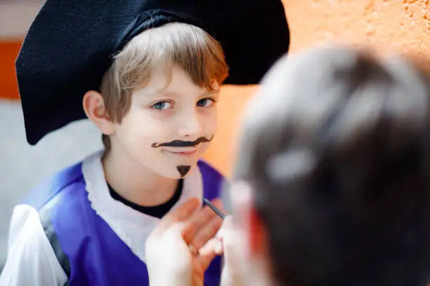 Father making face painting for little kid boy. Child dress up for carnival, Halloween or birthday party. Dad doing make up, drawing musketeer hero for son