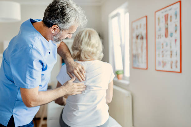 physiotherapeut untersucht einen senior-patienten mit rückenschmerzen - osteopathie fotos stock-fotos und bilder