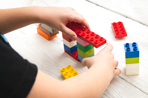 Close up of child's hands playing with colorful plastic bricks at the table.