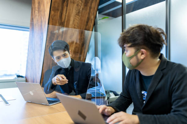 Two Asian businessmen having a meeting through the acrylic glass. At the conference room where taken countermeasure against infectious disease, two Japanese businessmen having a meeting. office cubicle mask stock pictures, royalty-free photos & images