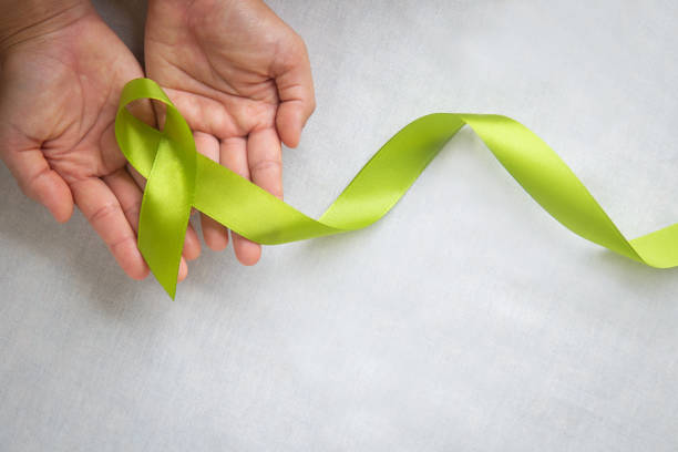 istock Hands holding light lime green ribbon on white fabric background with copy space. World Mental Health Day and Lymphoma Awareness symbol. Healthcare medical and insurance concept. 1289869560