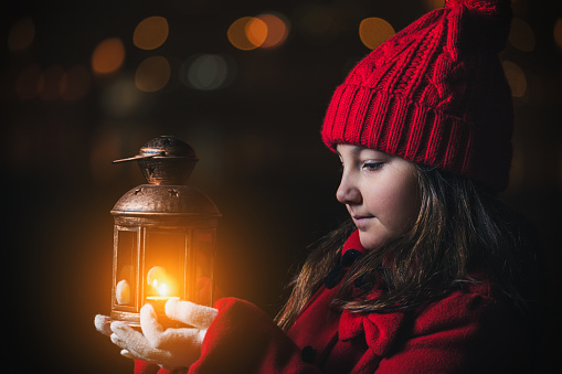 Beautiful little girl in a red winter coat holding vintage lantern outside