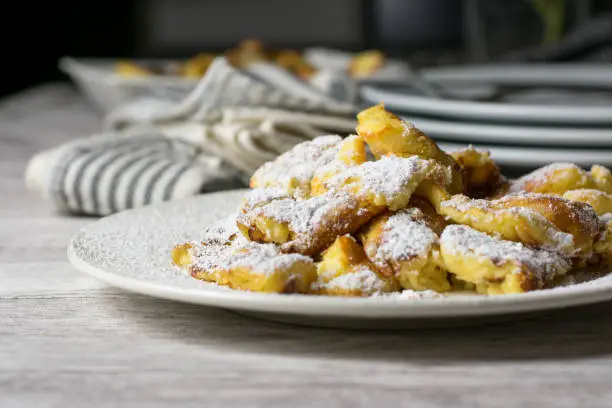 homemade baked austrian kaiserschmarrn with powdered sugar served on a white plate on kitchen table. Ready to eat