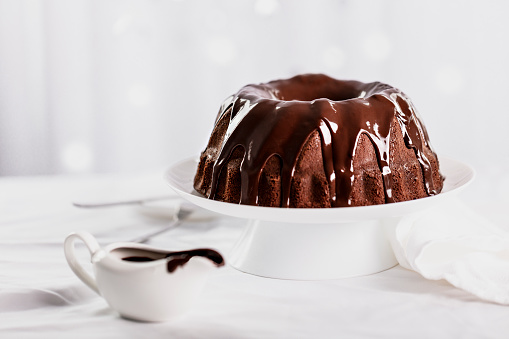 Dark chocolate cake covered with icing on a white stand. Selective focus