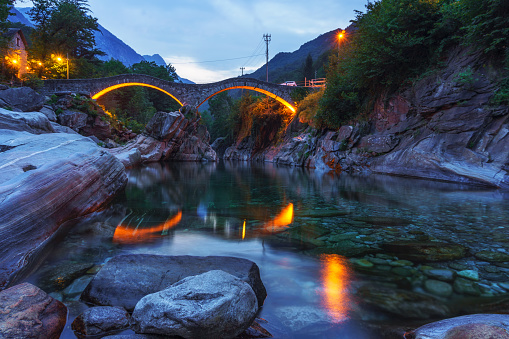 Double arch stone bridge at Ponte dei Salti in Lavertezzo, Canton Tessin, Switzerland, with the clear water of Verzasca river in the foreground. Photographed after sunset.