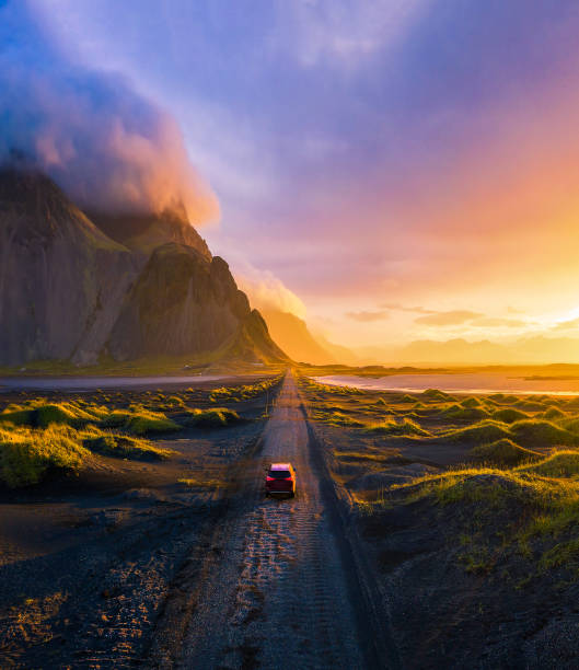 estrada de cascalho ao pôr do sol com montanha vestrahorn e um carro dirigindo, islândia - viagem em estrada - fotografias e filmes do acervo