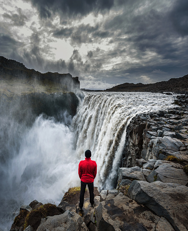 Young hiker standing close to the Dettifoss waterfall located on the Jokulsa a Fjollum river in Iceland. Dettifoss is the second most powerful waterfall in Europe after the Rhine Falls.