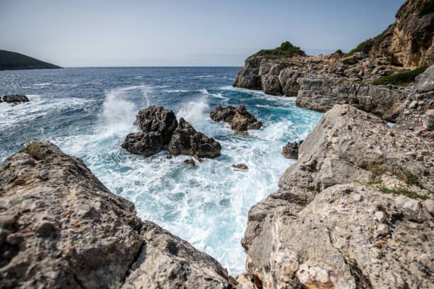 The ocean is rough and the waves are crashing against the rocks. The water is white and the rocks are brown