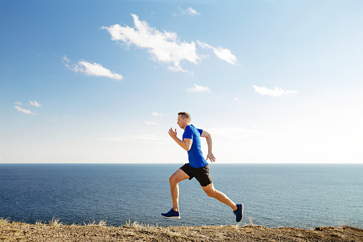 man mature runner running trail in background blue sky and sea