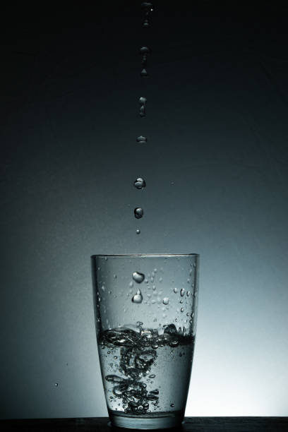 Water drops into a half glass of water in it with selective focus
