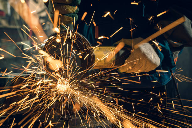 istock Locksmith in special clothes and goggles works in production. Metal processing with angle grinder. Sparks in metalworking 1289883547