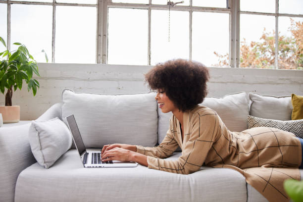 istock Smiling young woman lying on her sofa working on a laptop 1289886158