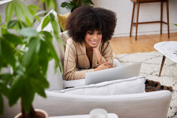 istock Smiling young woman watching something on a laptop while relaxing on her sofa 1289886795