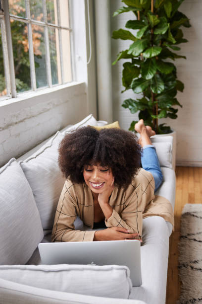 istock Smiling young woman lying on her sofa watching something on a laptop 1289886989