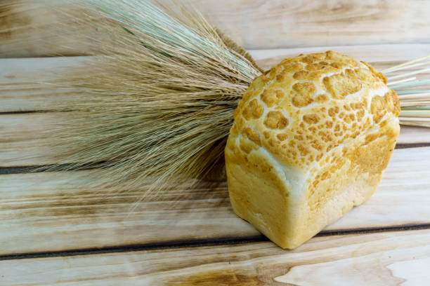 Bread brick and a bunch of wheat spikelets on a wooden background. Square wheat light loaf of bread with pattern on top