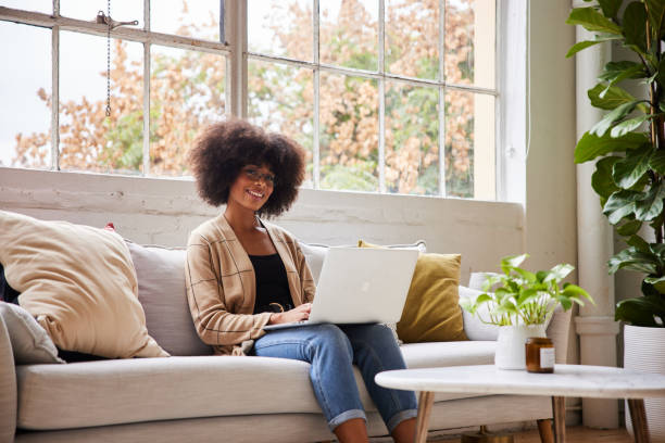 istock Smiling young woman working on a laptop on her sofa 1289887821