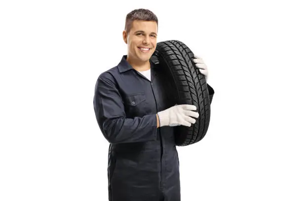 Auto mechanic worker carrying car tire on shoulder and smiling at camera isolated on white background