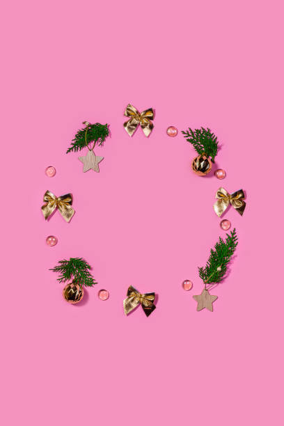 istock vertical pink festive background, copy space. Christmas decorations are laid out in the shape of a wreath: golden bows, balls, branches, wooden stars, crystals 1289894633