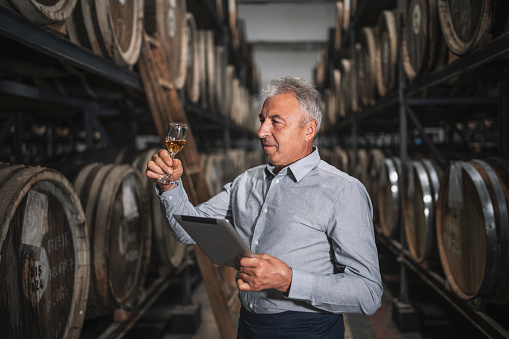 Senior man inspecting aged whiskey in cellar.