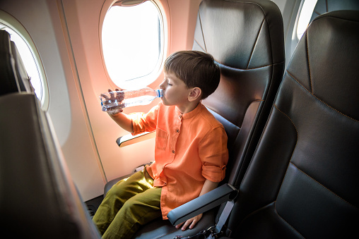 Charming kid traveling by an airplane. Little boy drinking water during the flight. Air travel with little kids.