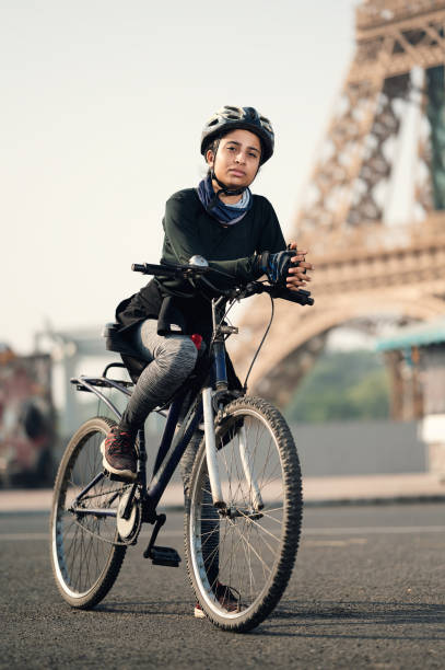 Portrait of a fit Indian female cyclist out of a training ride near Eiffel tower. She is wearing sportswear, hand gloves and helmet. Photographed in a modern contemporary style, color, vertical format with some copy space.