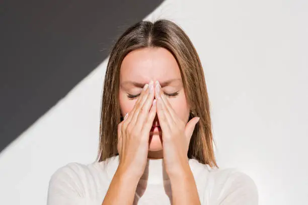 Photo of Woman feeling unwell, painful headache because of sinus ache, sinusitis, sinus pressure. Sad woman holding her nose and head because sinus pain. Coronavirus symptoms