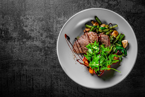 Roastbeef salad with green beans and mushroom in a bowl on Dark grey black slate background