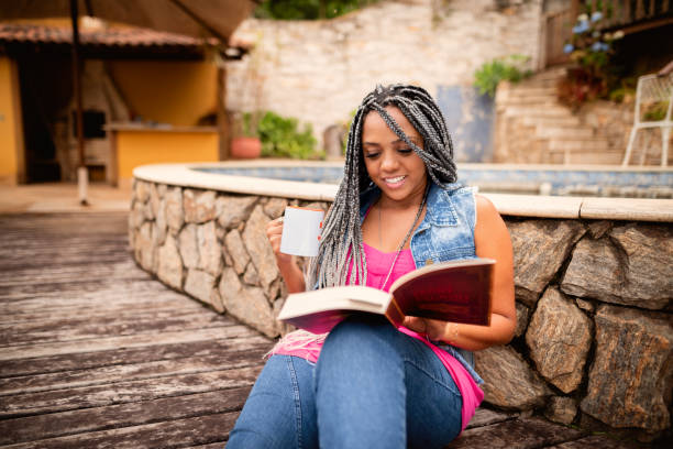 Black woman, sitting on the floor, relaxing and reading a book in the back yard