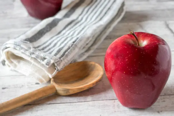 beautiful red apple on a table with wooden spoon and towel.