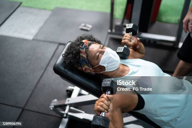 Senior woman using face mask doing exercise with dumbbell in the gym