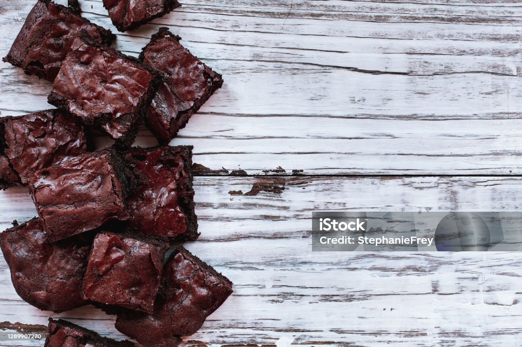 Squares of delicious, homemade fudgy brownies stacked a white rustic wooden table background Squares of delicious, homemade fudgy brownies stacked a white rustic wooden table background. Image shot from top view overhead. Brownie Stock Photo