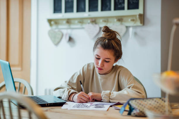 So Much Homework A teenage girl from the North East of England sitting in the kitchen of her family home working her way through the homework she needs to complete for school the following day. homework table stock pictures, royalty-free photos & images